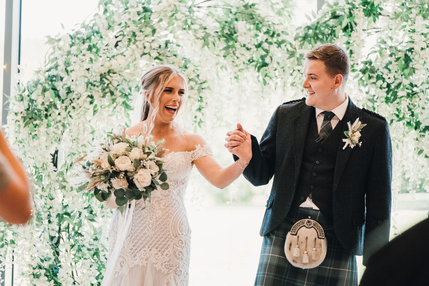 A couple celebrates during their Scottish wedding ceremony under floral decorations.