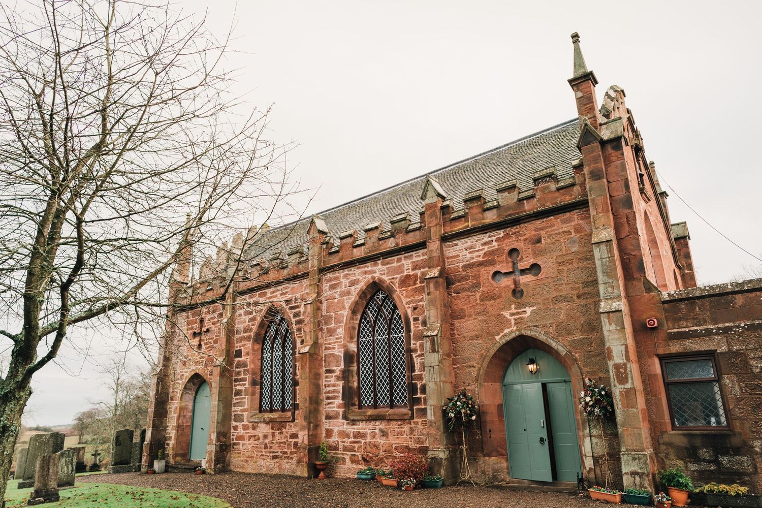 Historic red sandstone church with Gothic windows and green door surrounded by bare winter trees.