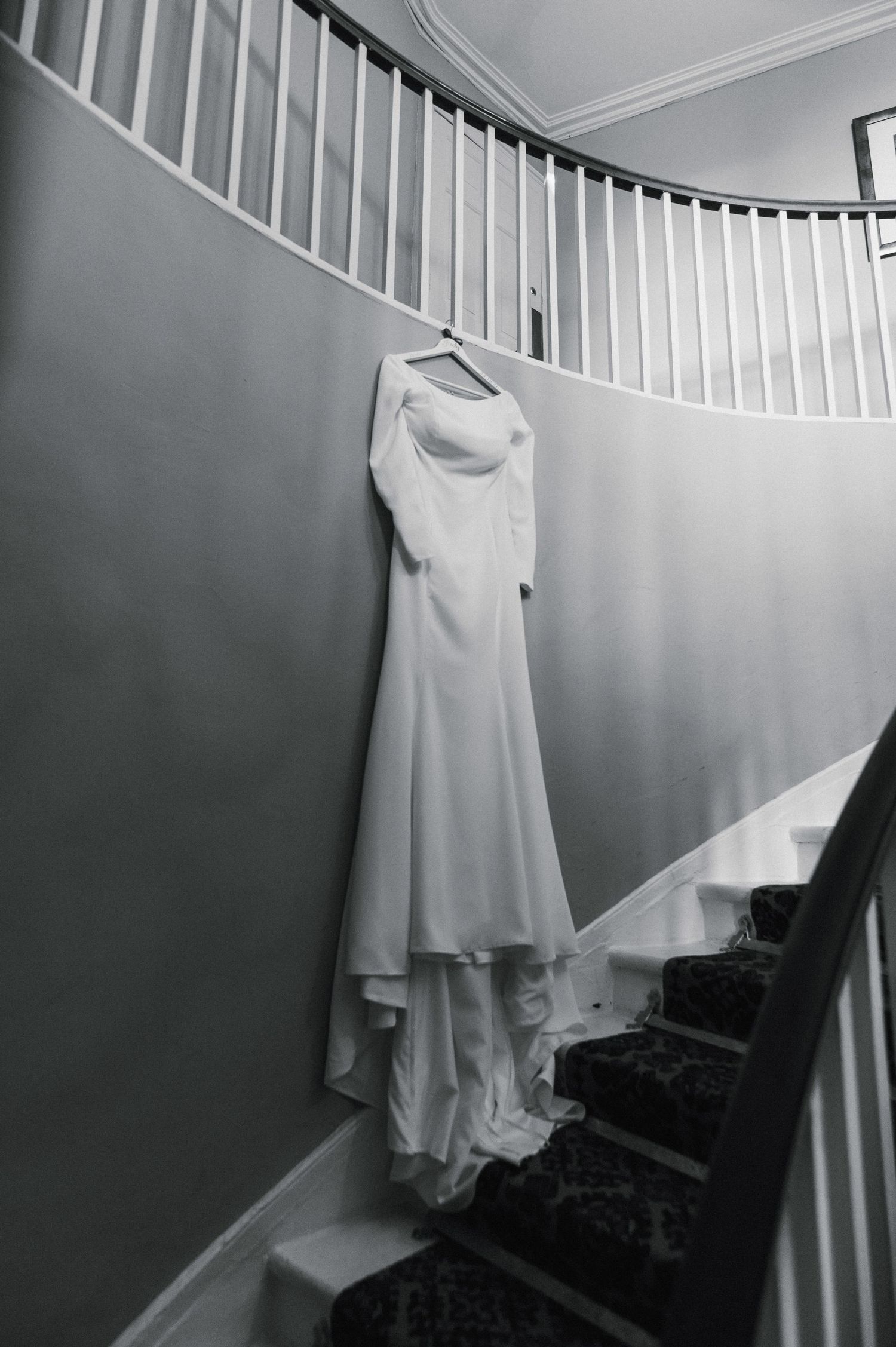 Elegant white wedding dress hanging on curved staircase wall in black and white.
