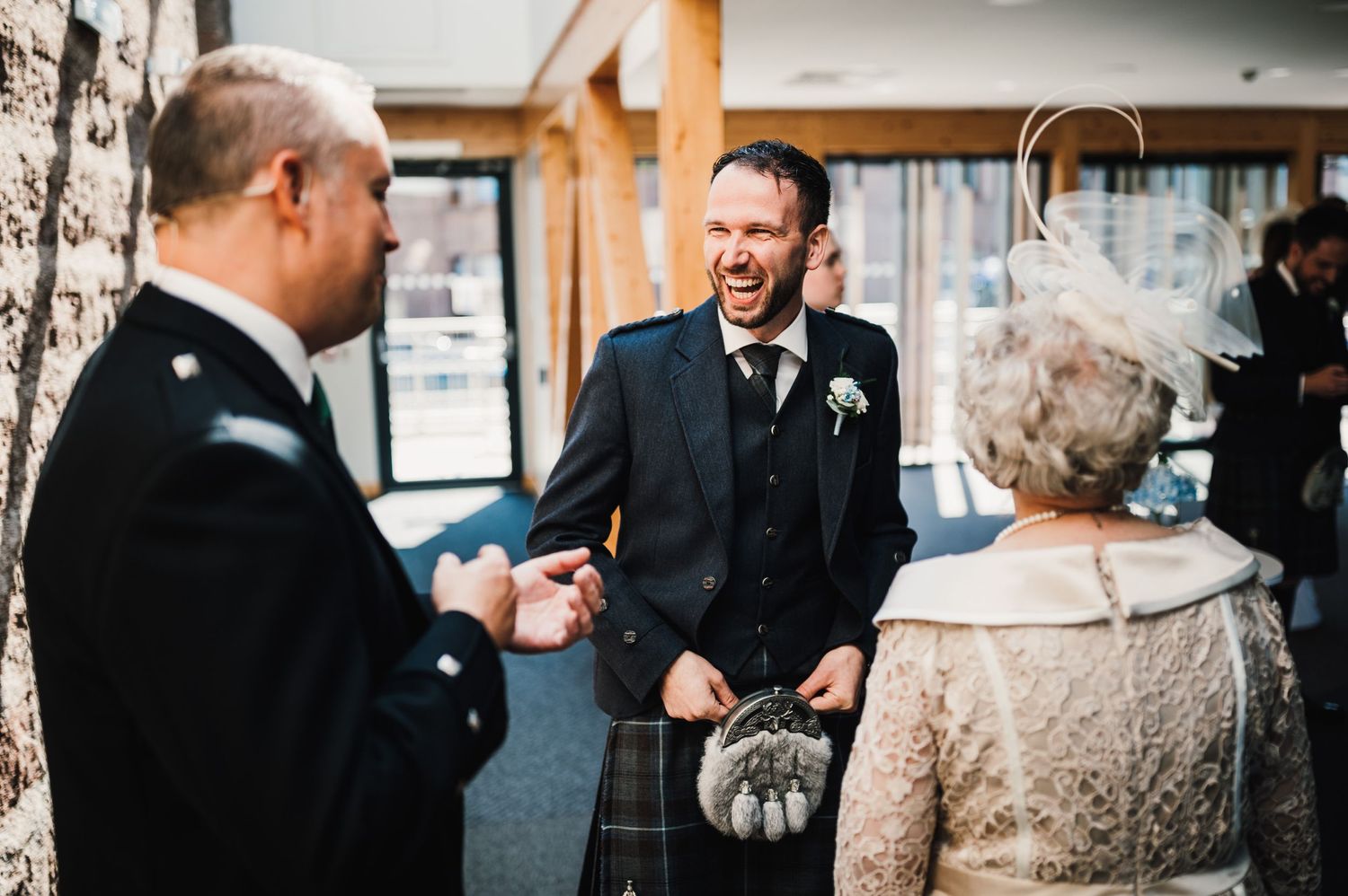 Wedding guests share a joyful moment in candid conversation wearing traditional Scottish kilts.
