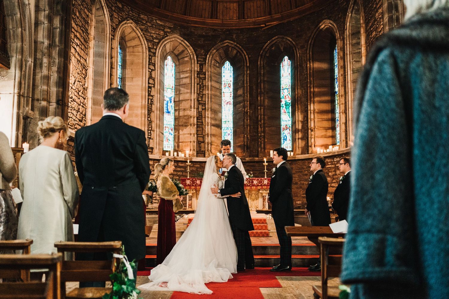 A traditional church wedding ceremony takes place inside a grand cathedral with ornate stained glass windows and brick architecture.