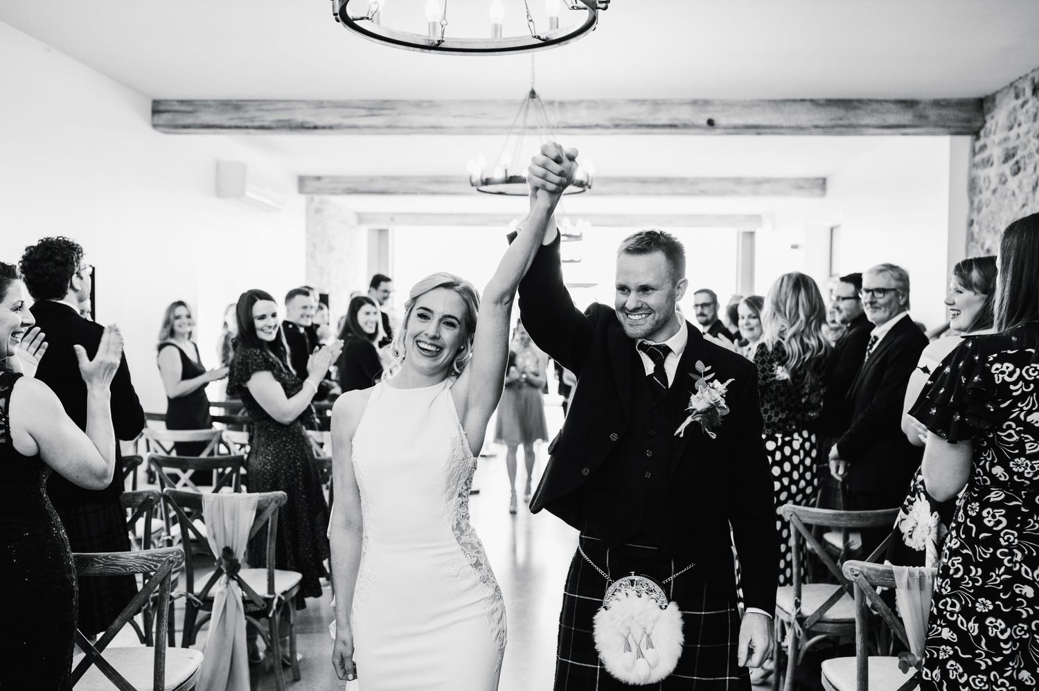 Celebratory moment at wedding reception with couple raising hands in victory under chandelier.