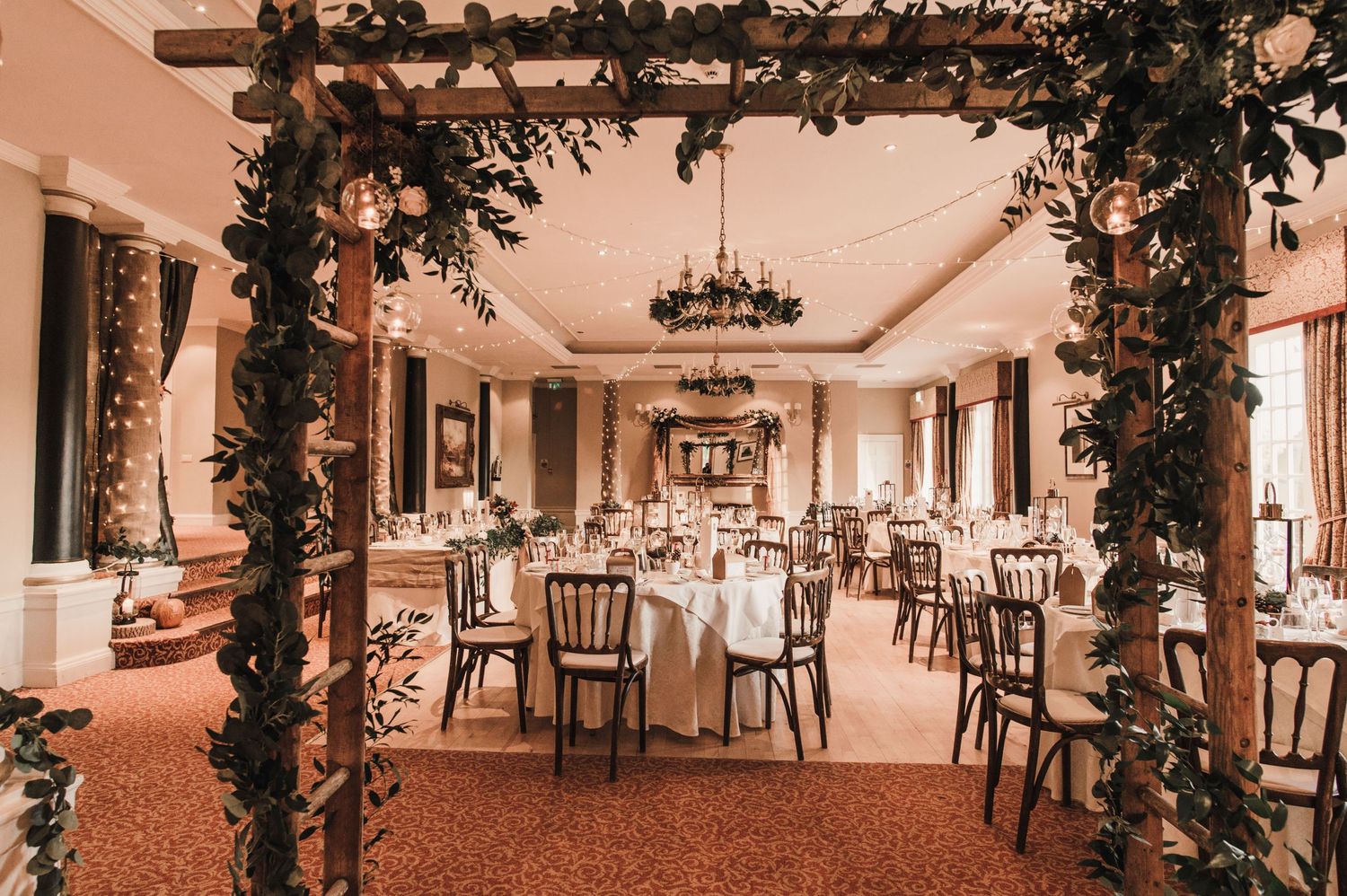 An elegant reception hall with floral arch decorations and beautifully set round tables.