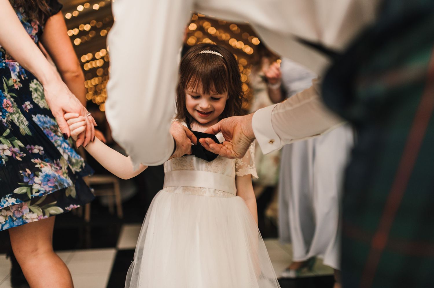 Young flower girl in white dress dances at wedding reception under warm lighting.