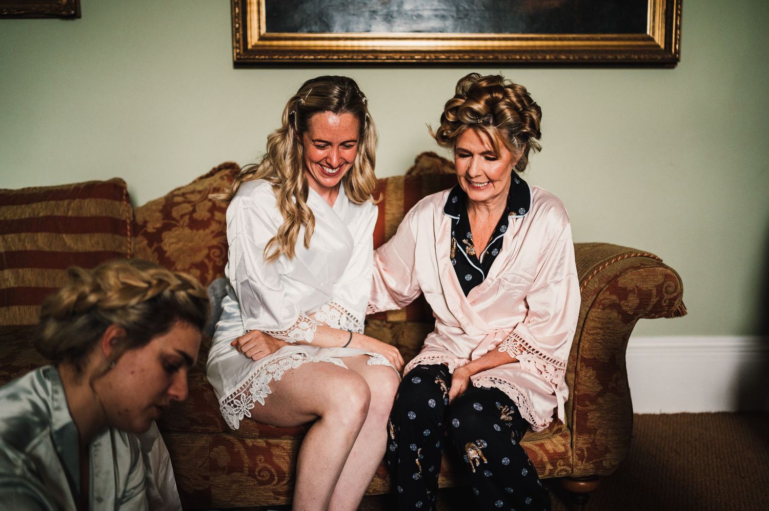 Two people in robes share a laugh while sitting on a couch indoors.