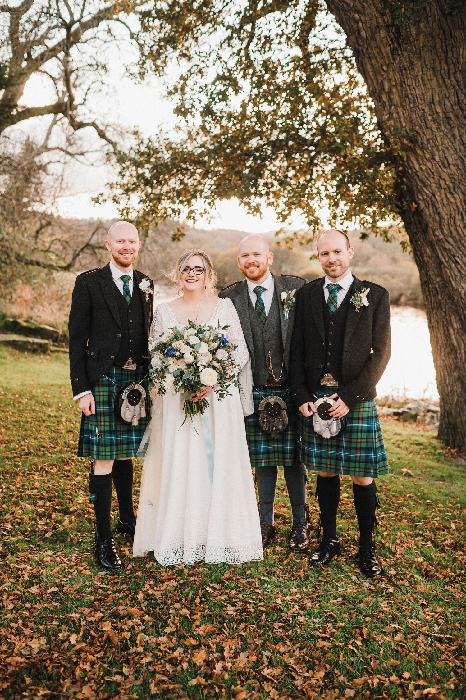 Traditional Scottish wedding photo with men wearing kilts standing on autumn leaves.