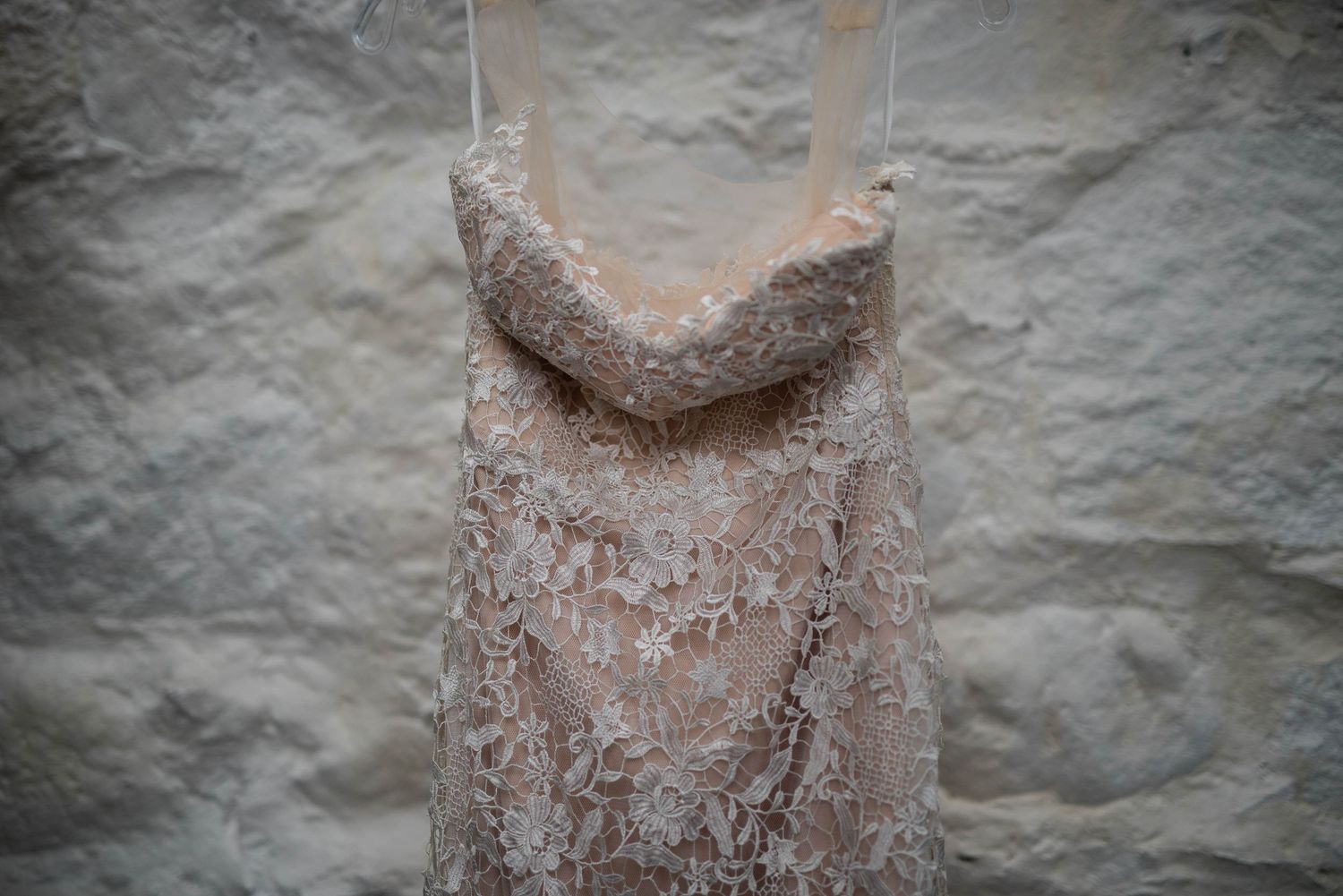 Close-up detail of lace wedding dress bodice hanging against white wall.