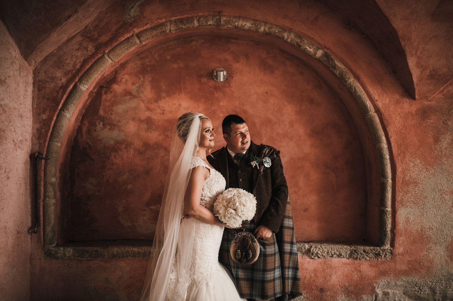 A wedding moment captured under a dramatic arched passageway with warm lighting.