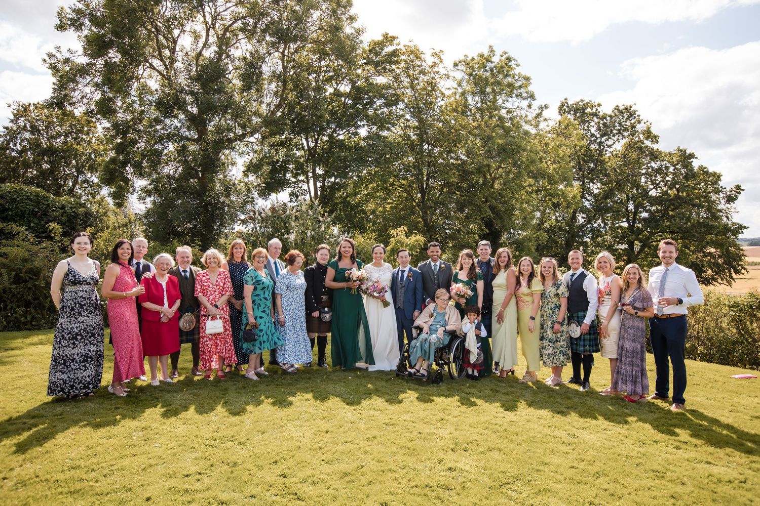 Large wedding party group photo taken outdoors on a grassy hill during golden hour.