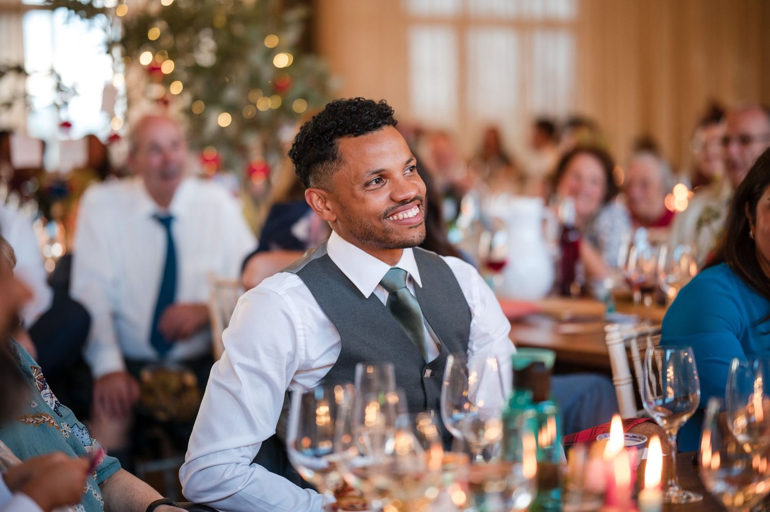 A well-dressed guest smiles warmly at an elegant wedding reception with table settings and decorations.