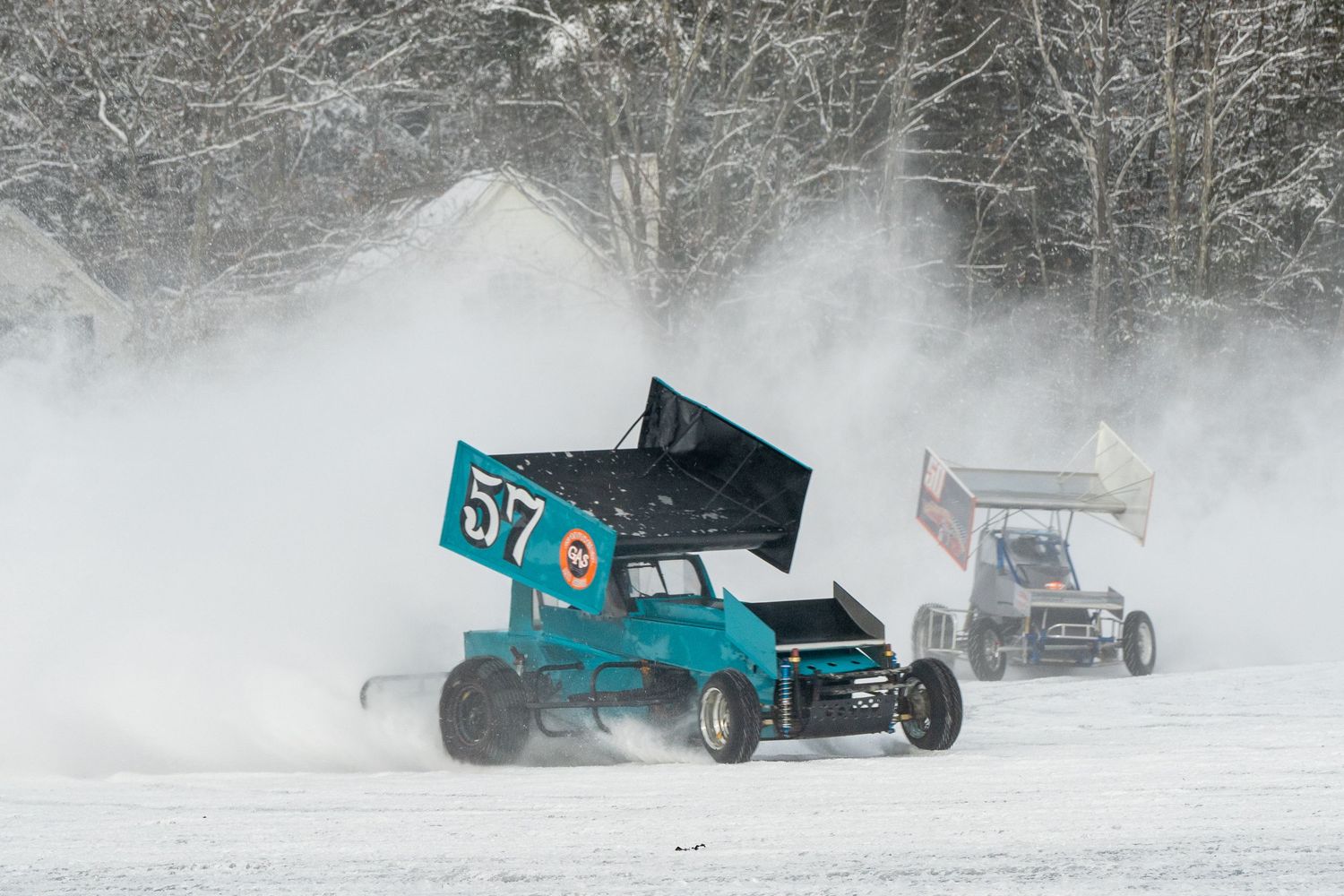 Race cars slide and drift through snowy conditions creating dramatic powder sprays.