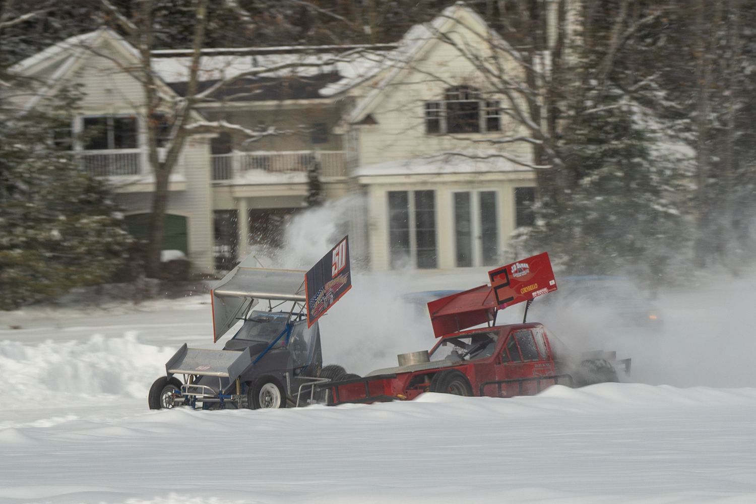 Race cars kick up snow while competing in a winter motorsport event on a snowy track.