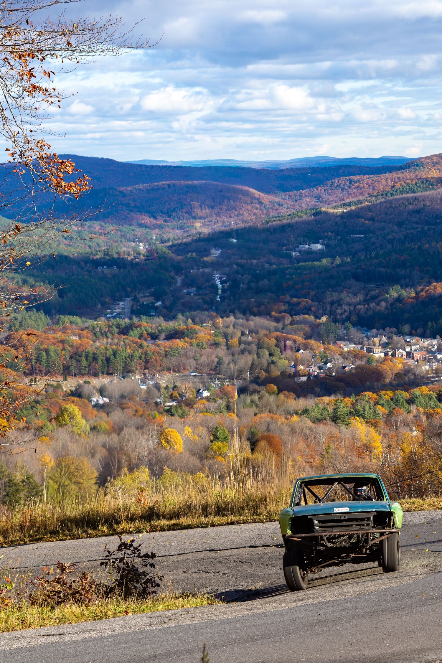 Classic race cars competing on a mountain course with stunning fall foliage and valley views.