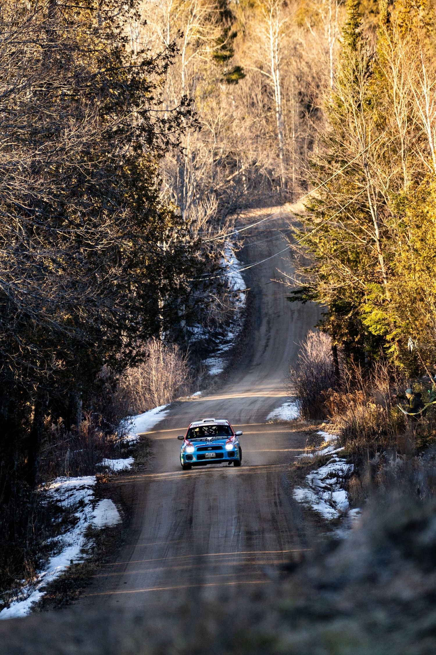Rally car races through snowy forest road with dramatic winter scenery.