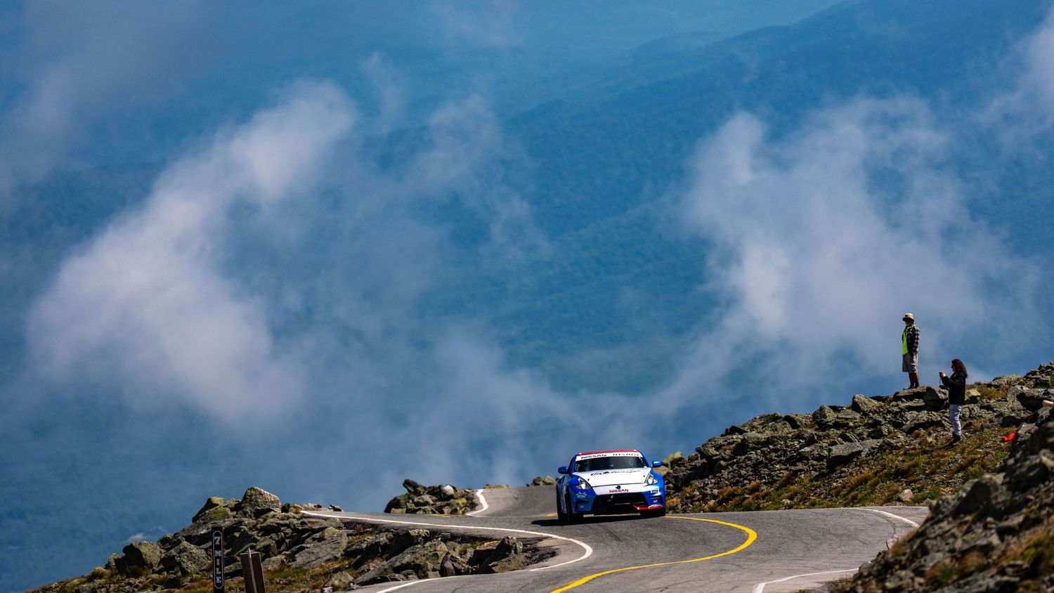Blue sports car racing on a winding mountain road above the clouds at Pikes Peak Hill Climb.
