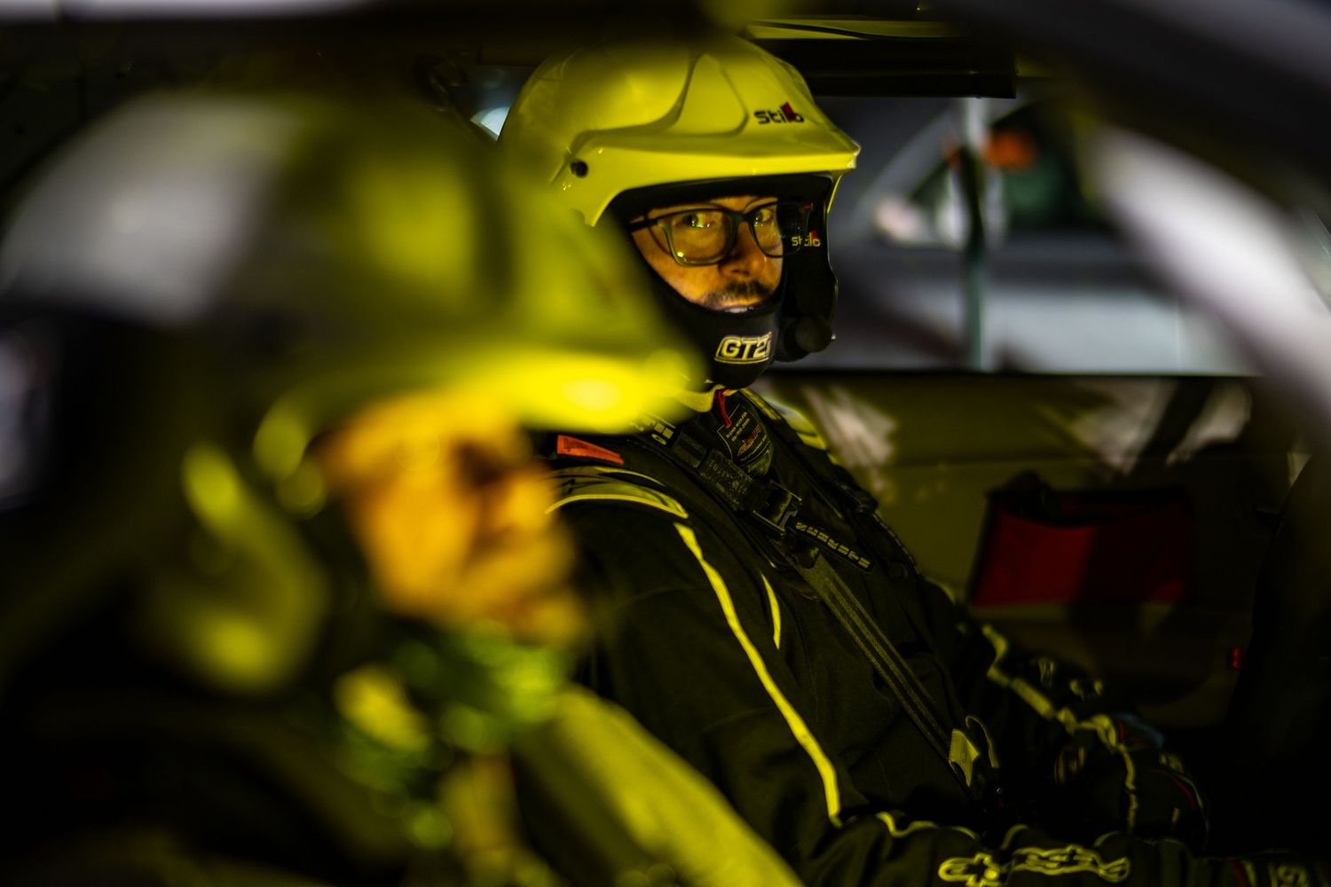 Racing helmet visible through car window with yellow ambient lighting.