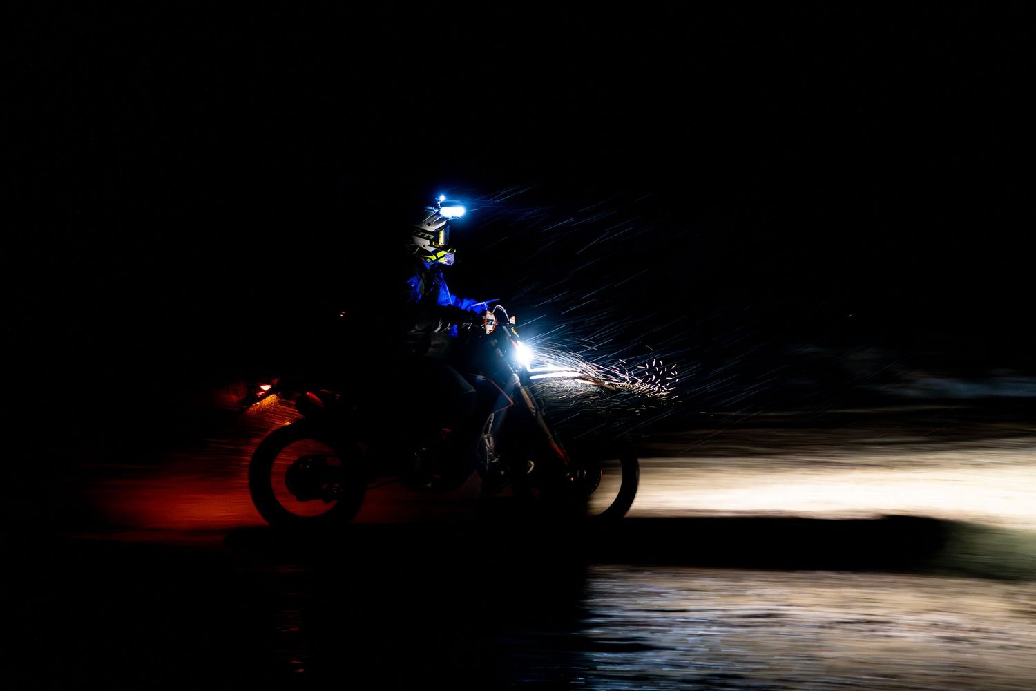 Motorcycle creates light trails while racing through darkness on forest trail.