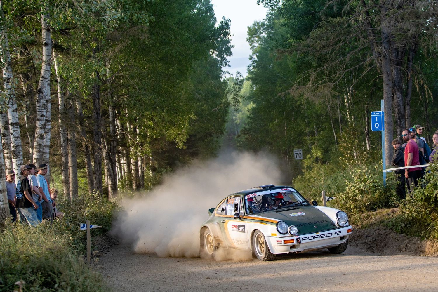 Rally cars kick up dust while racing through a forested course during a competitive event.