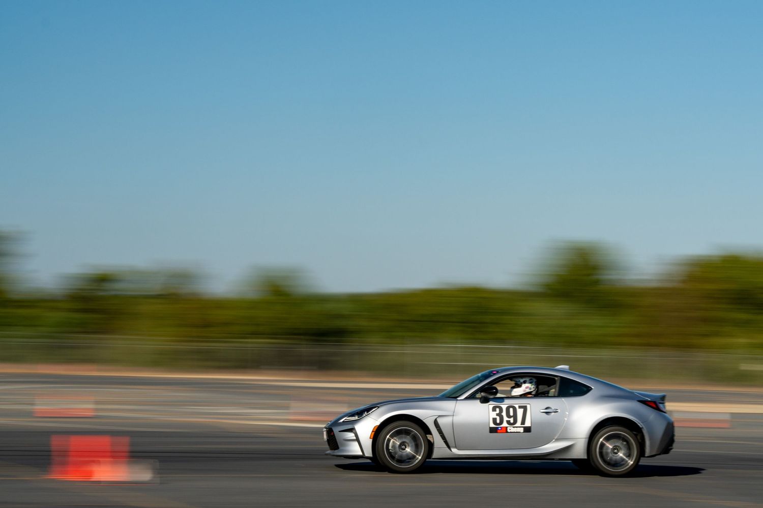 High-performance vehicles racing around orange cones on a paved track under blue skies.