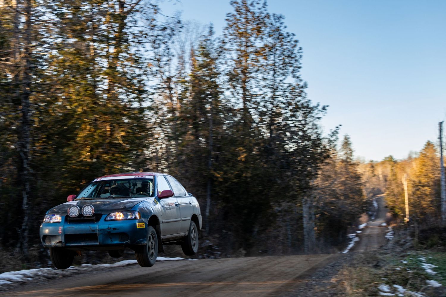 Blue Subaru rally car catches air on forest rally stage.