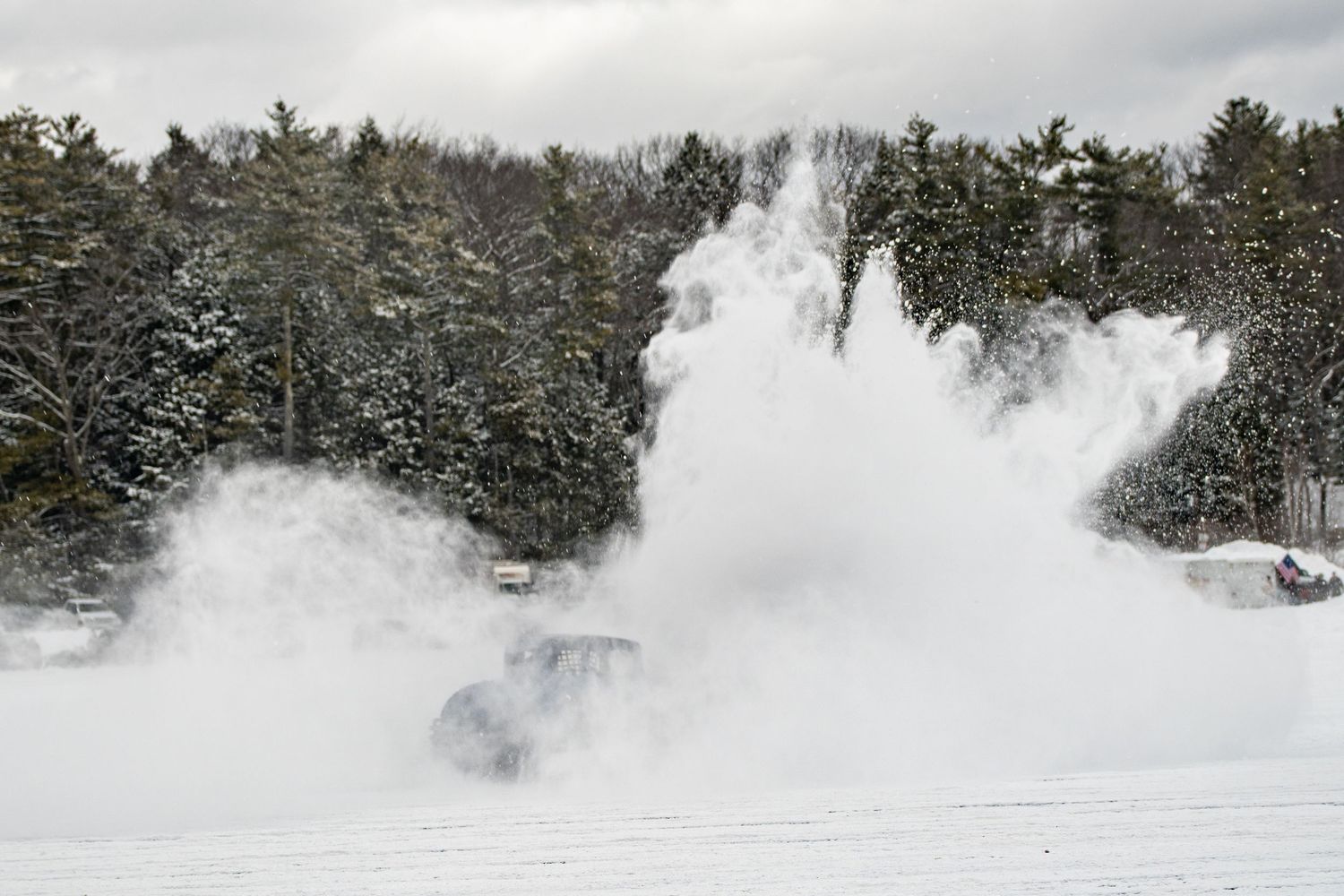 Performance cars creating dramatic snow plumes while racing on a frozen course.
