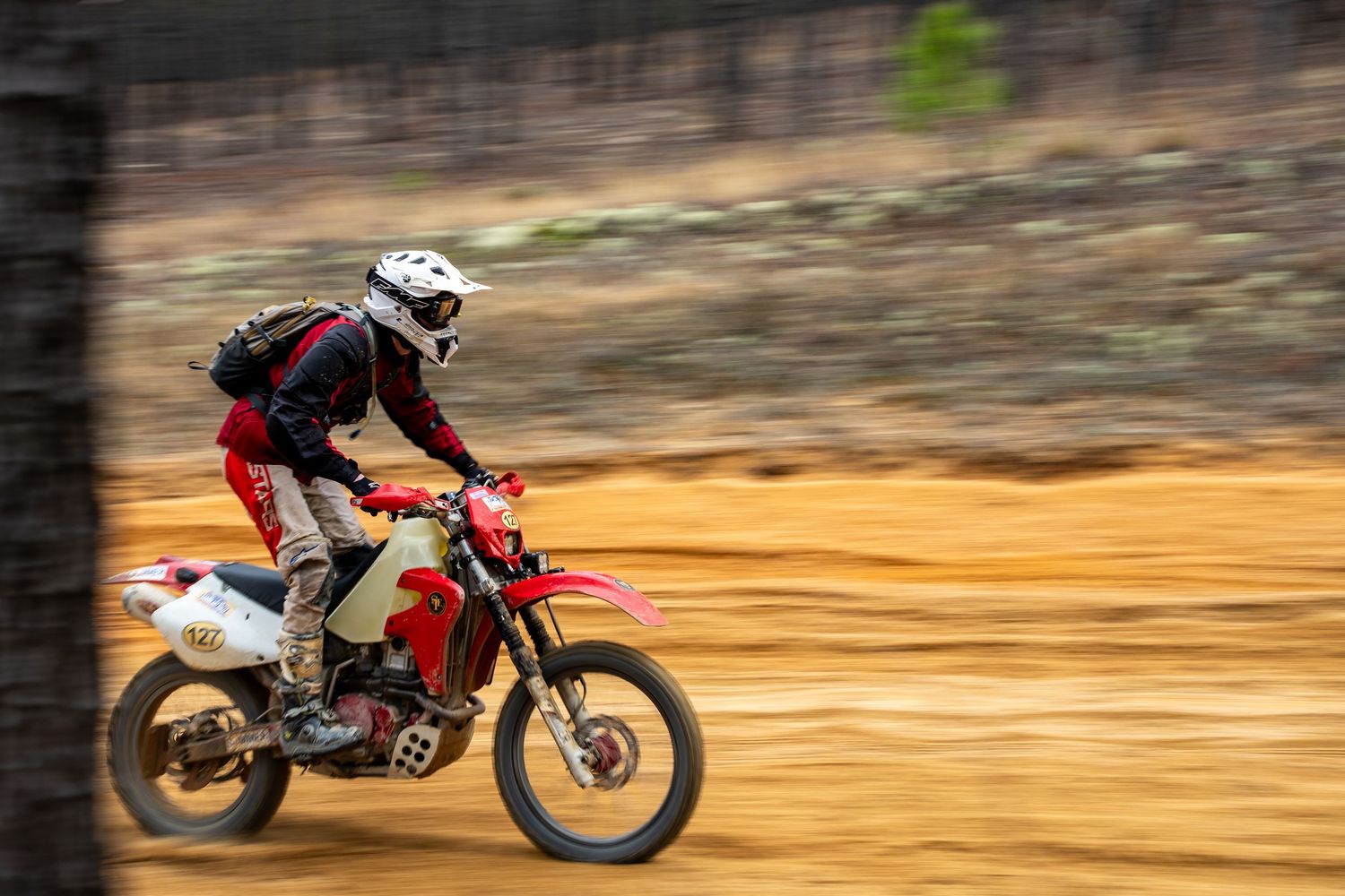 Dirt bike rider performing sequential jumps on a dusty off-road track during sunset.