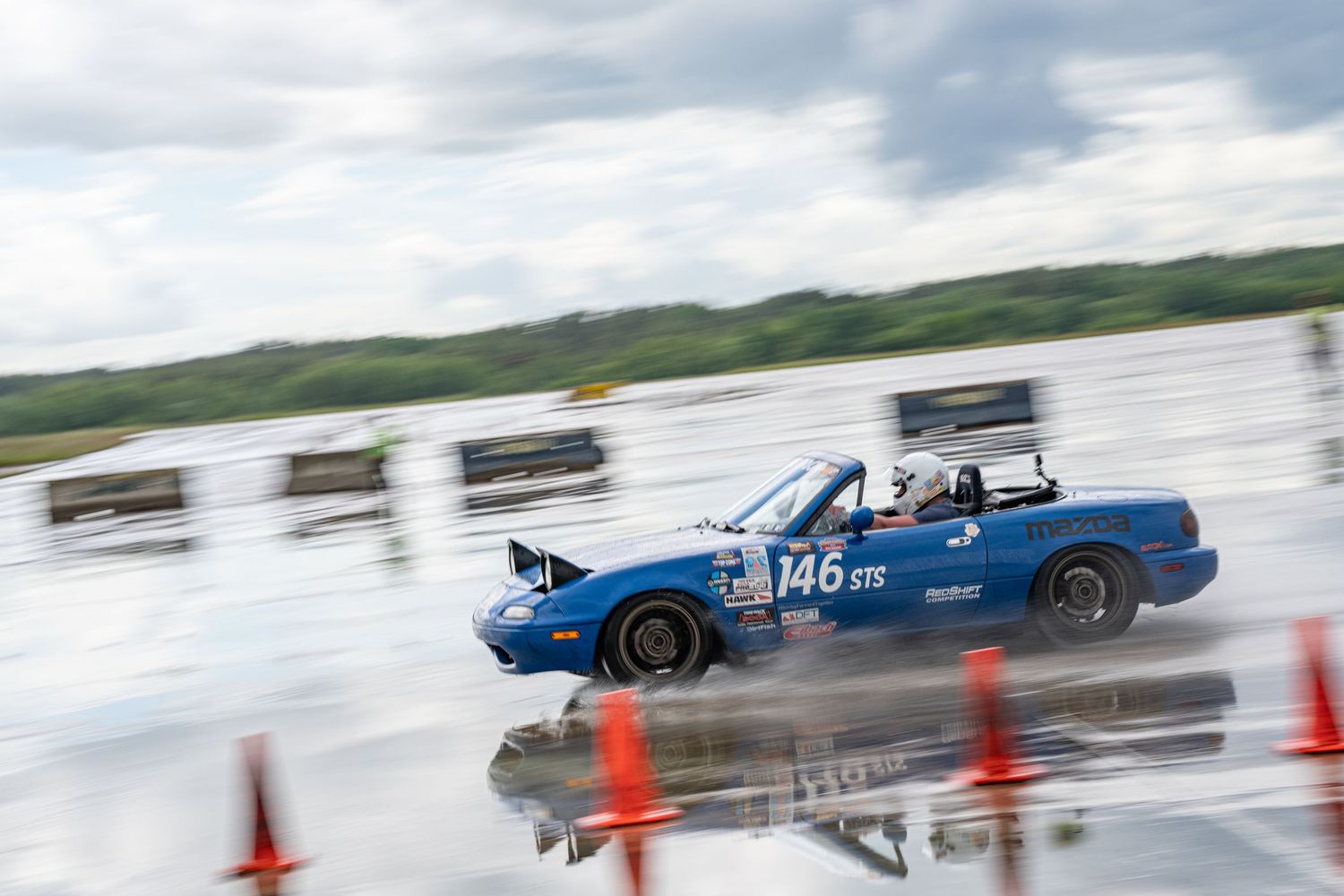 Blue race car performing high-speed maneuvers through orange cones on a wet track.