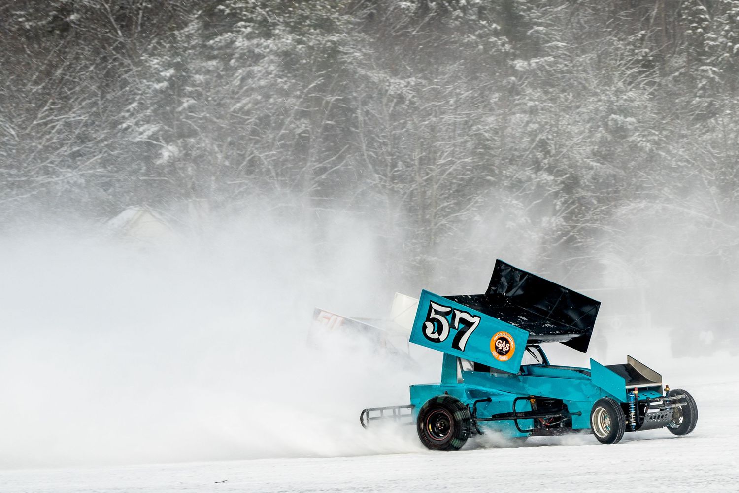 Race car drifting through snowy conditions creating dramatic powder spray.