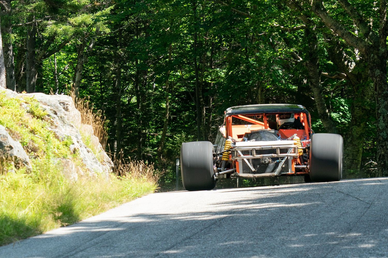An open-wheel race car takes a corner at speed on a mountain road course.