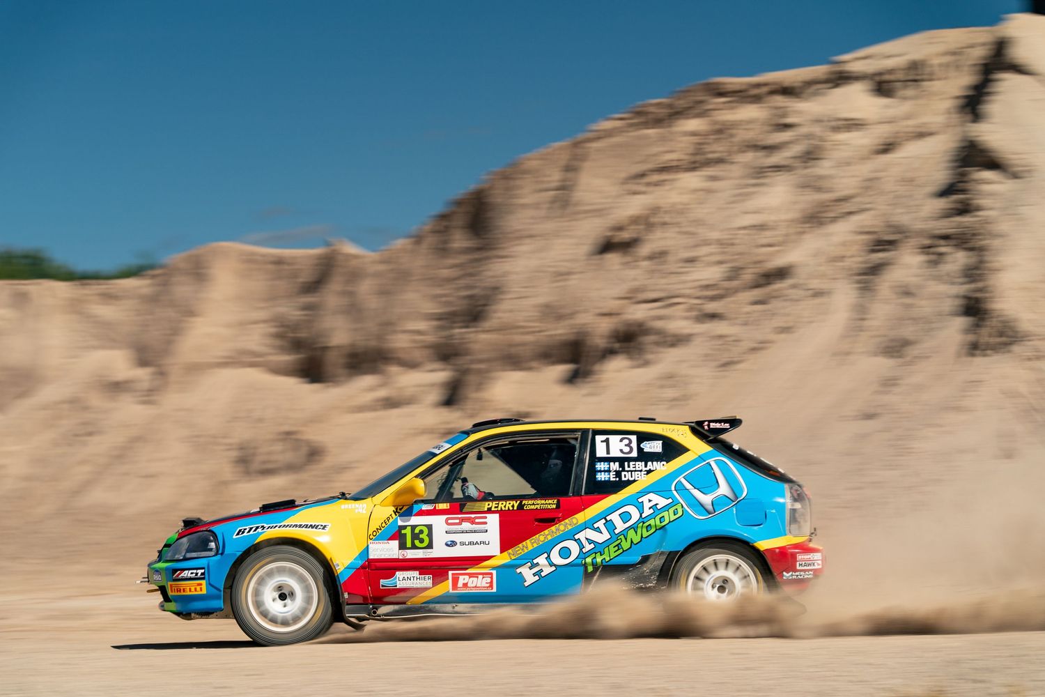 Rally car racing through desert terrain with colorful racing livery.