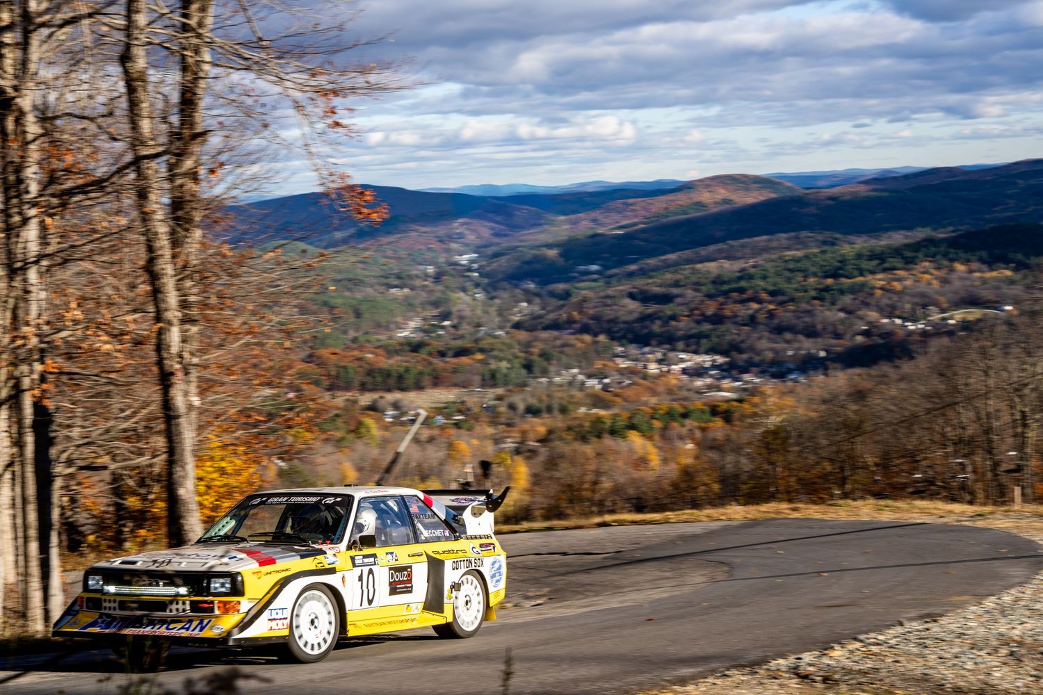 Rally cars racing along a mountain road with spectacular valley views and autumn colors.