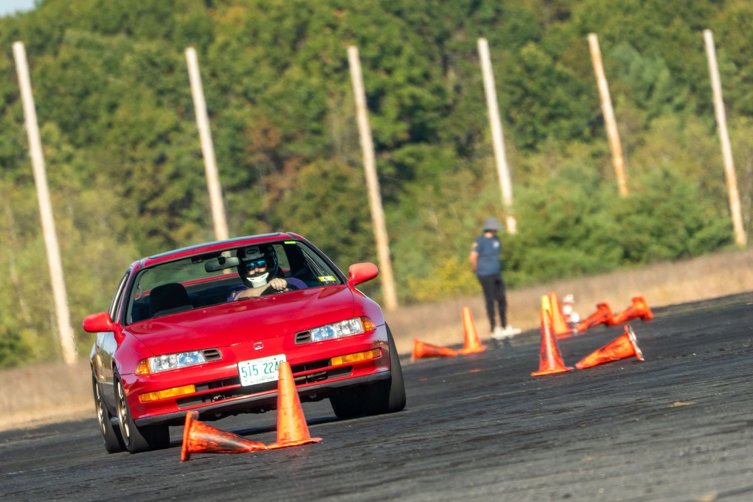Multiple sports cars competing in an autocross event marked by orange cones.