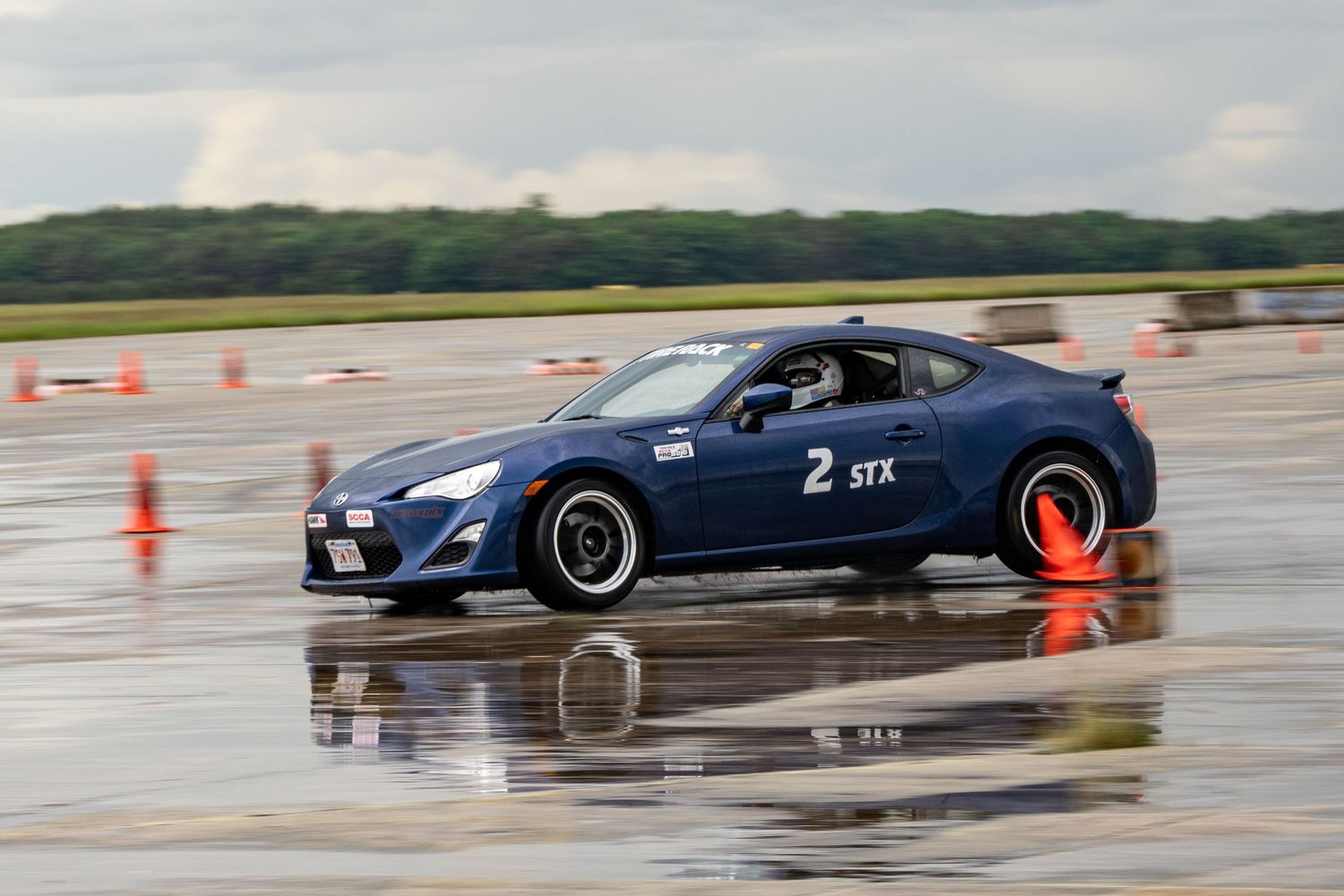 Performance cars lined up on a wet track with orange cones for autocross racing.