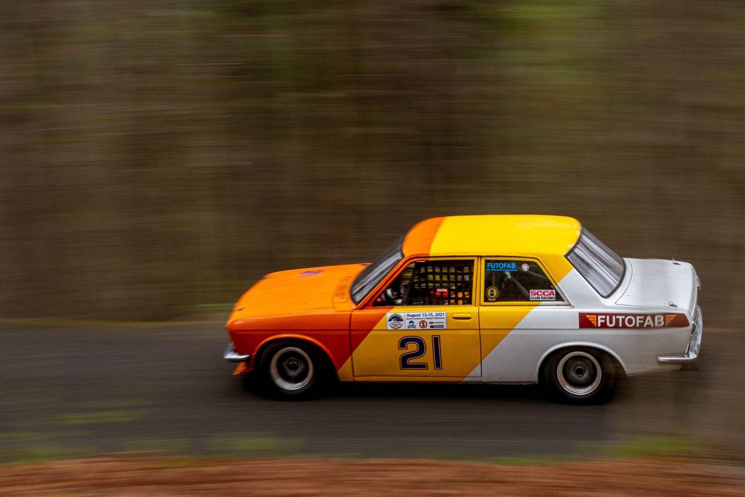 Orange and white number 21 FUTOFAB rally car racing on a forest road with motion blur background.