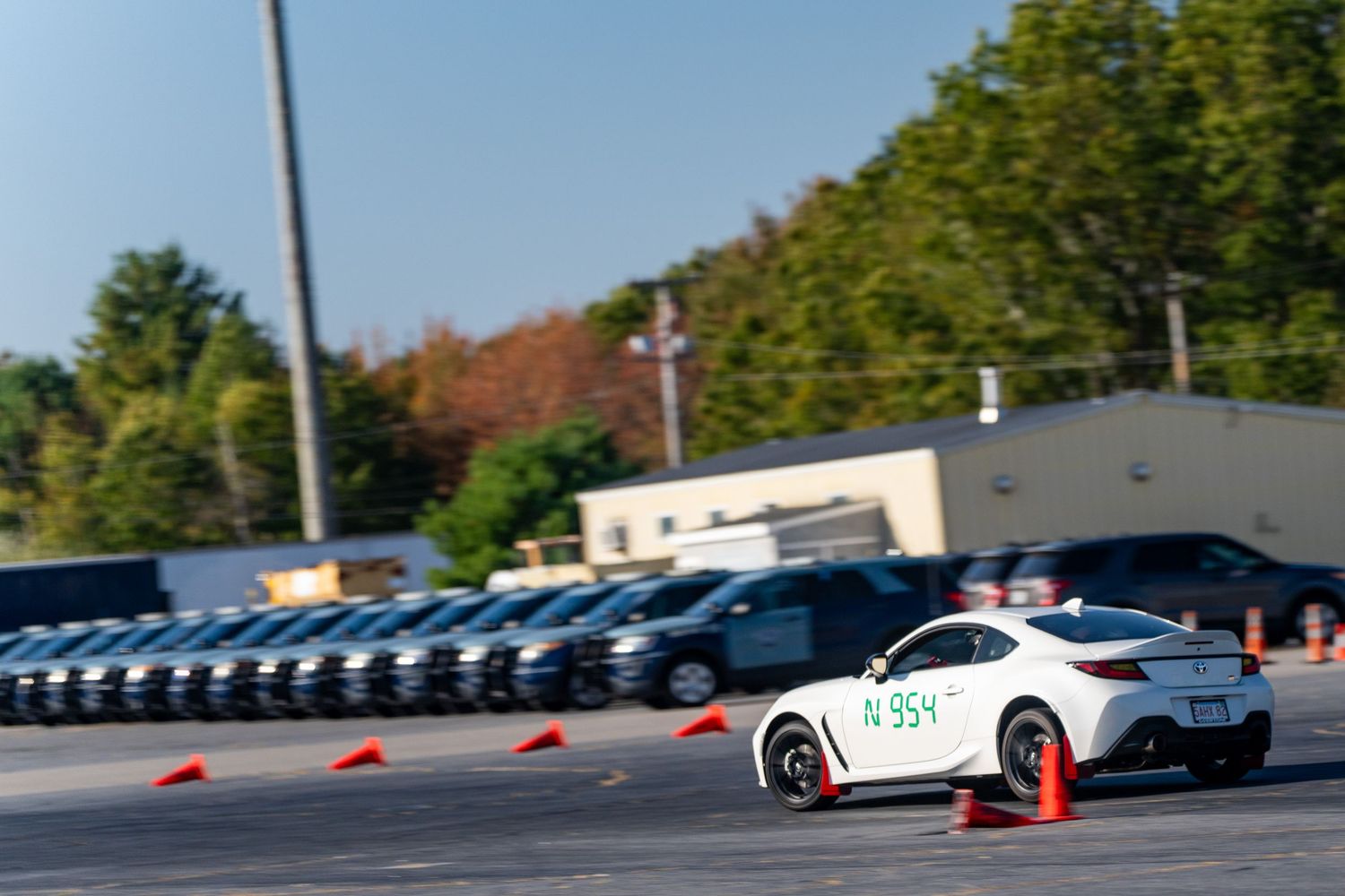 Sports cars maneuvering through a cone-marked autocross course in a parking lot.