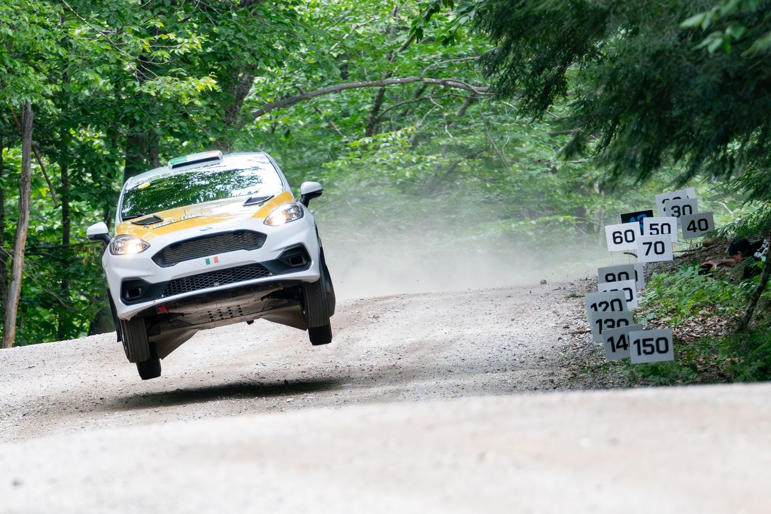Rally car catching air while jumping over a dirt road hill.