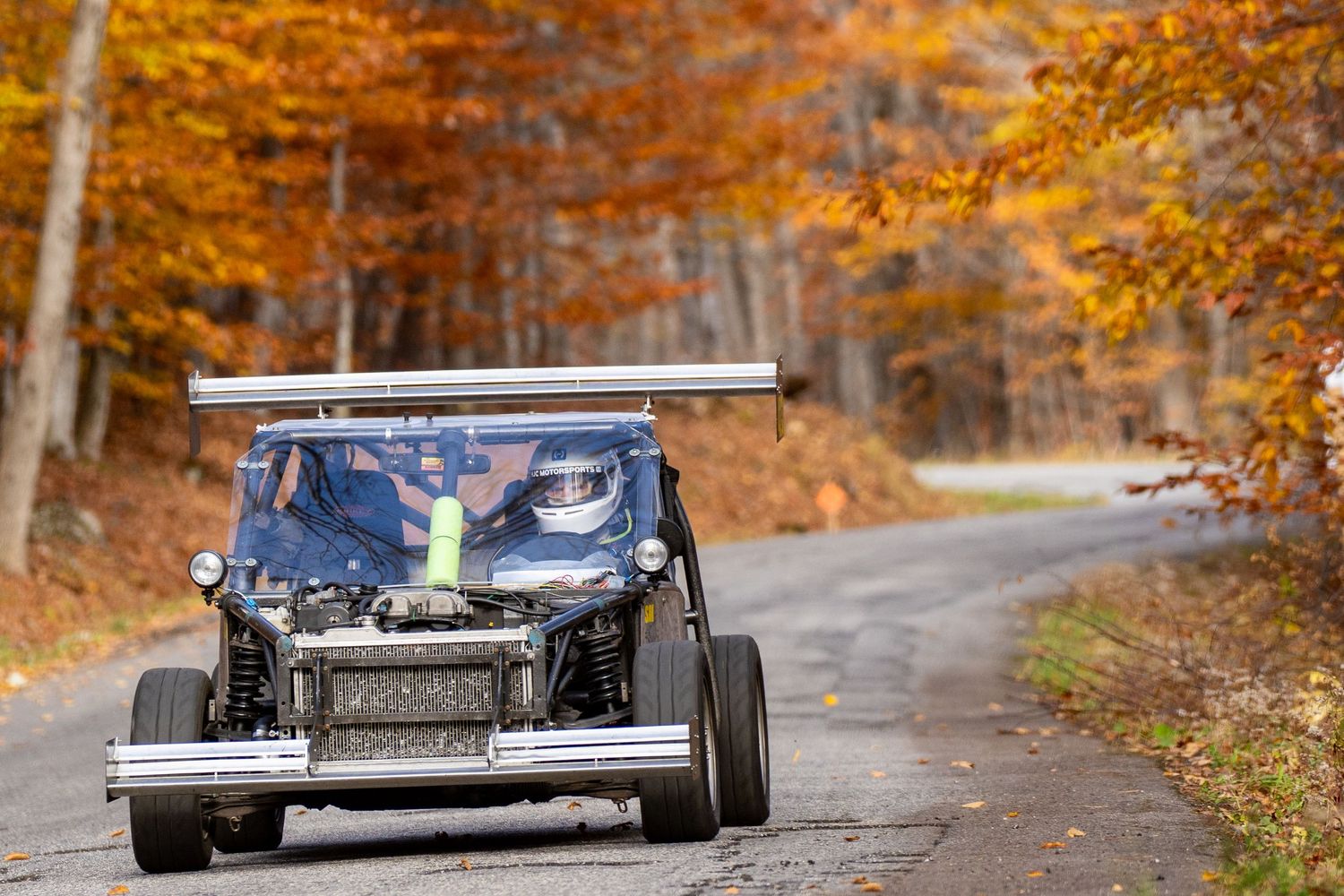 Sports cars racing on an autumn road lined with vibrant orange fall foliage.