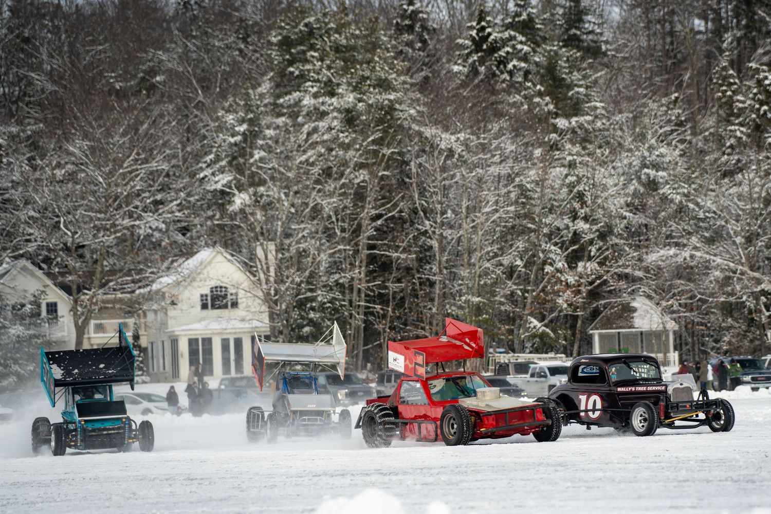 Multiple race cars compete on a snow-covered track near residential homes.