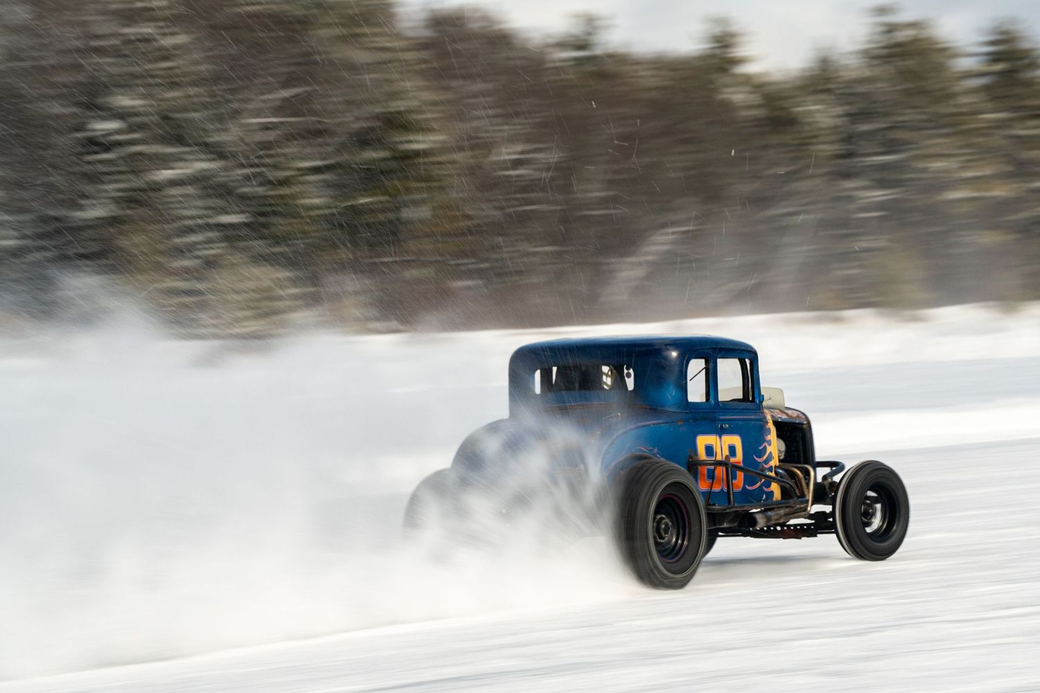Modified race cars speed through a snowy course creating dramatic powder clouds.