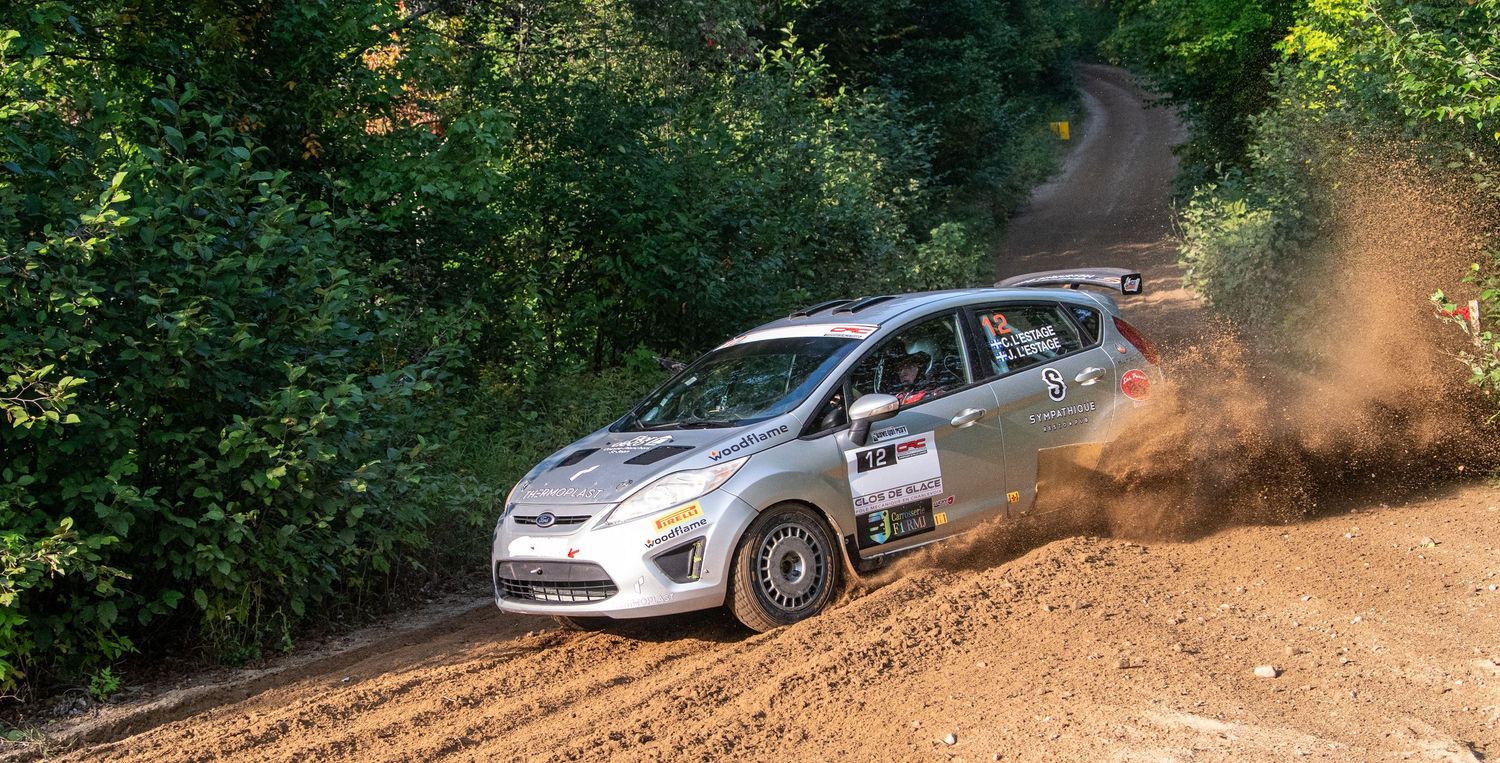 Rally car racing through a forest trail with dust flying during an intense competition.