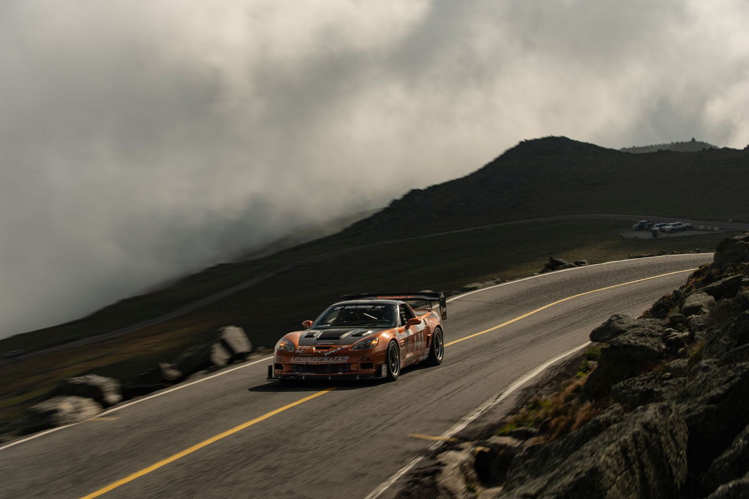 A race car speeds along a winding mountain road under dramatic cloudy skies at Pikes Peak Hill Climb.