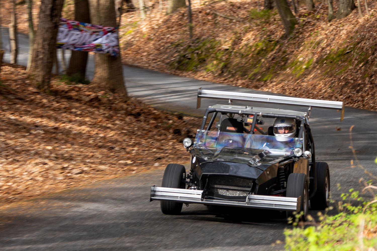 Black vintage open-wheel race car with large rear wing navigating a tree-lined racing circuit.