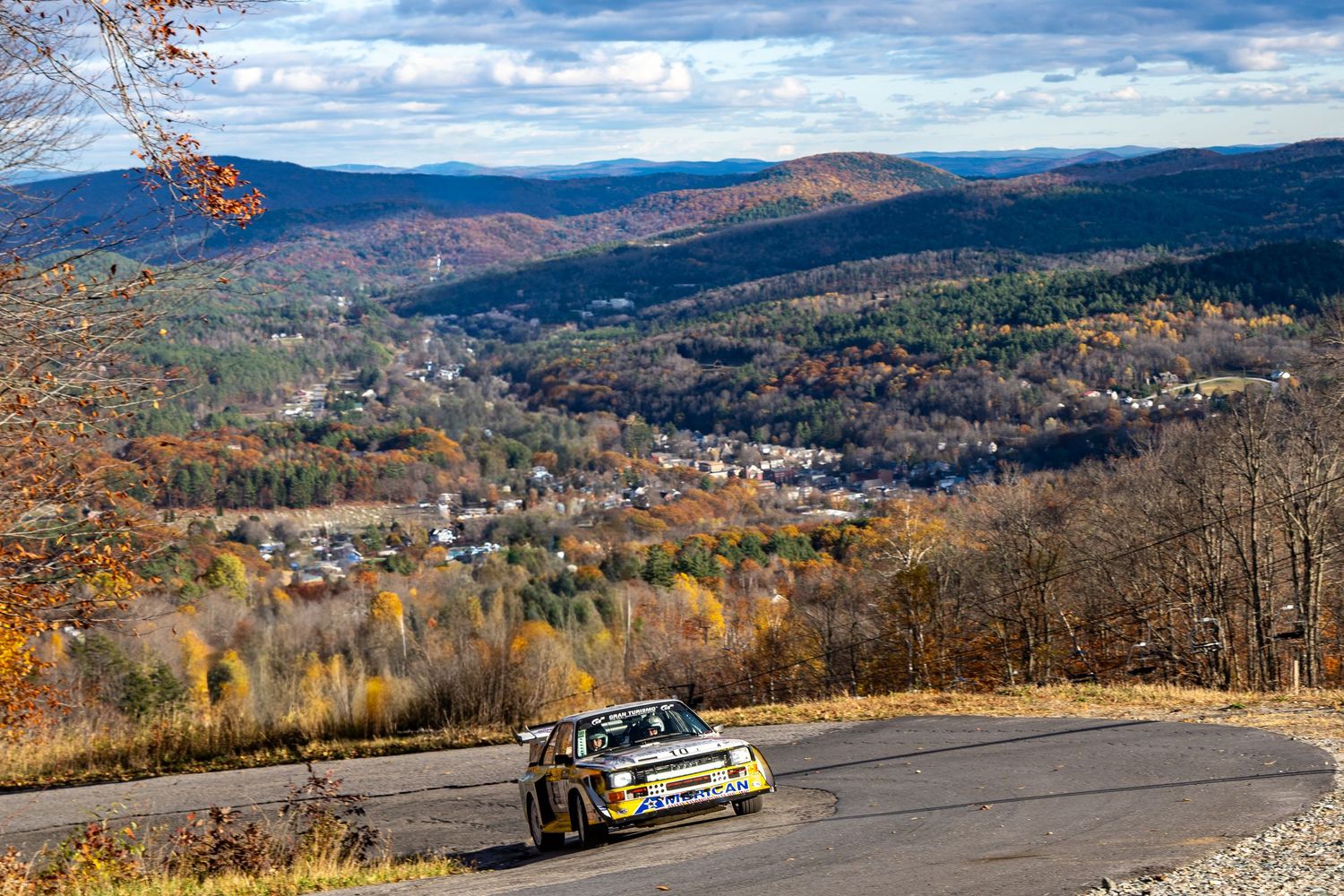 Performance cars racing on a scenic mountain road with panoramic valley views.