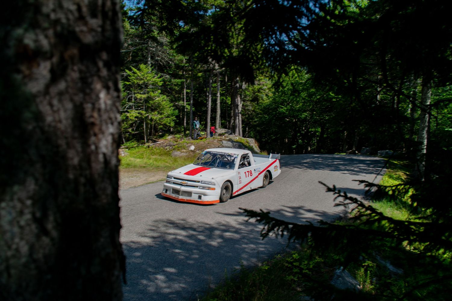 Sports car racing through a winding mountain road surrounded by dense forest.