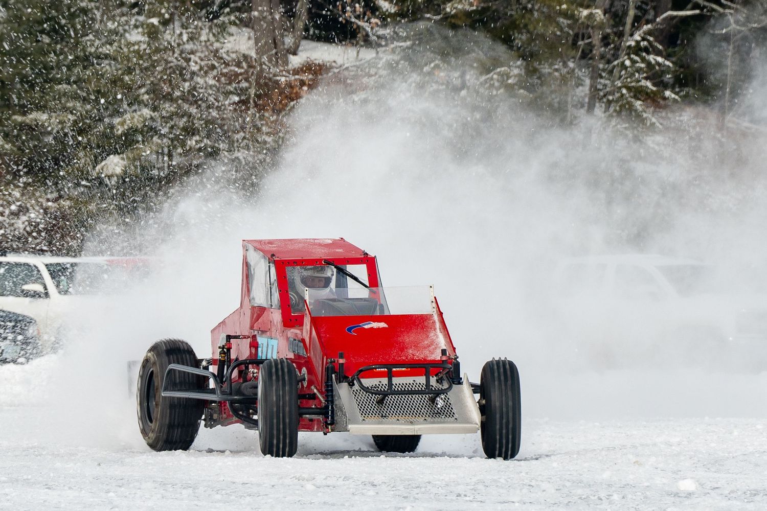 Vintage hot rods racing through deep snow on a winter track.