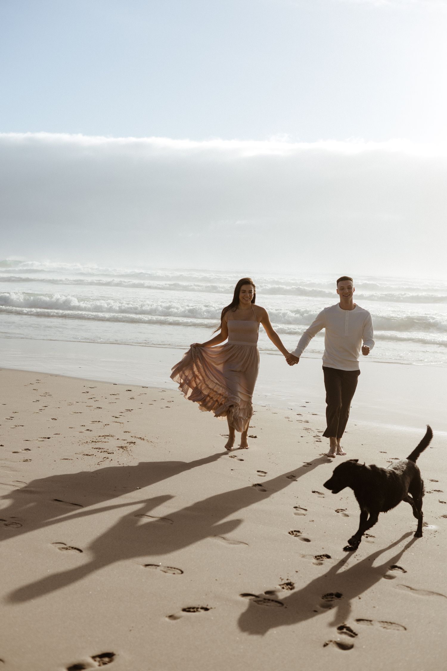 PNW wedding photographer beach session with couple and their dog running into ocean together oregon coast beach