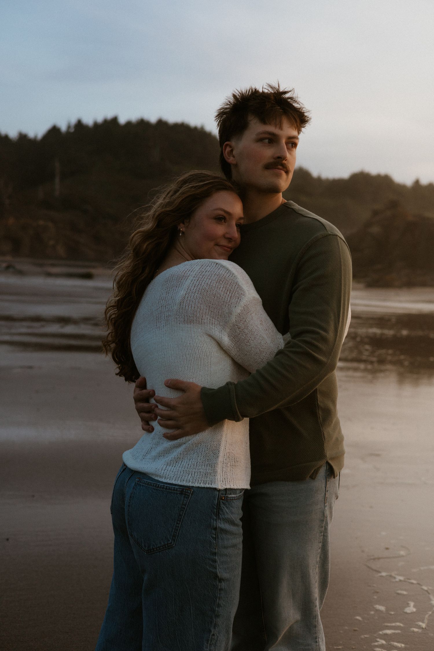 Oregon Coast beach sunset couples photoshoot couple hugging and looking out into the ocean taking it all in together.