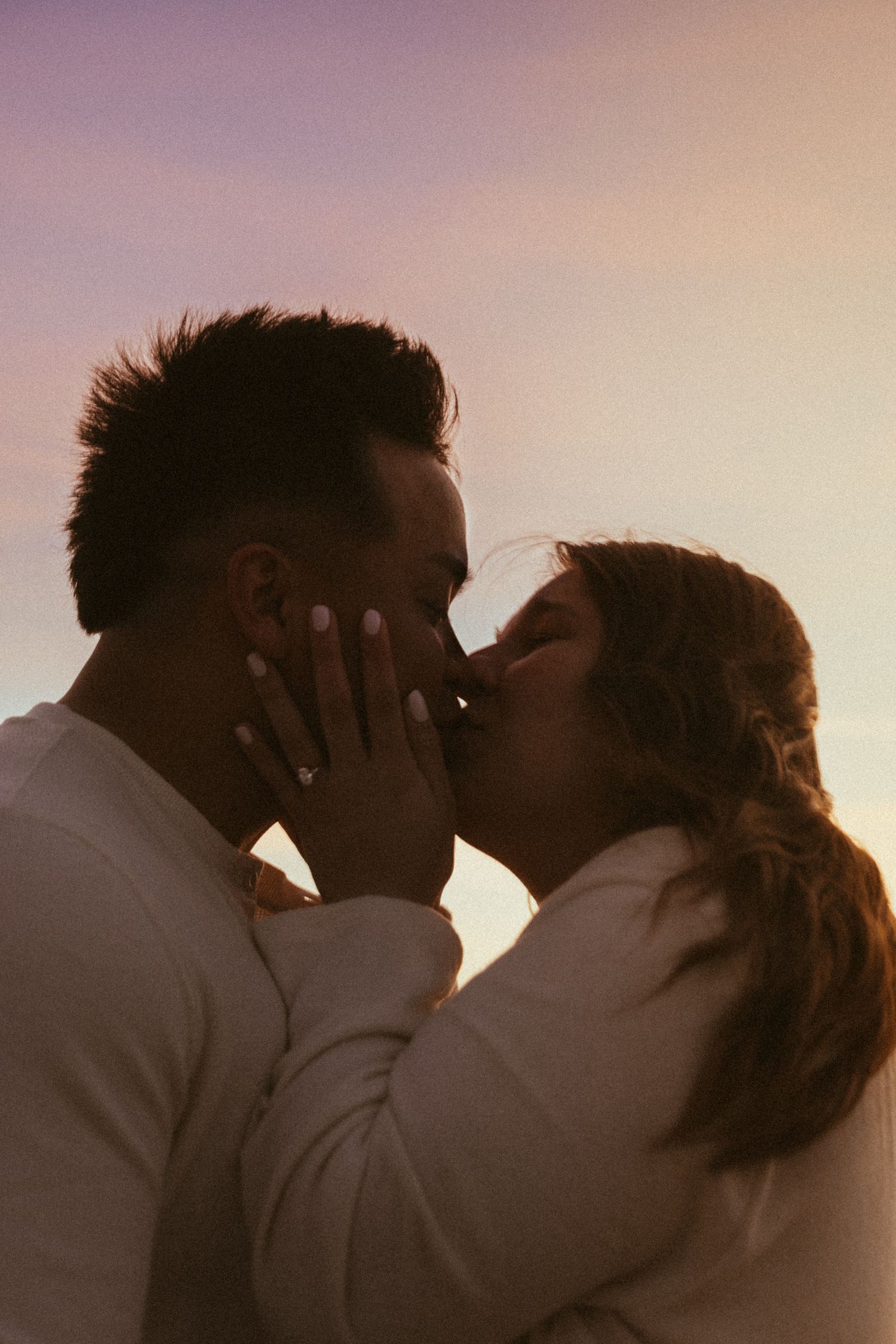 Blue hour engagement photoshoot on the Oregon Coast, close up of ring with couple kissing in the background.