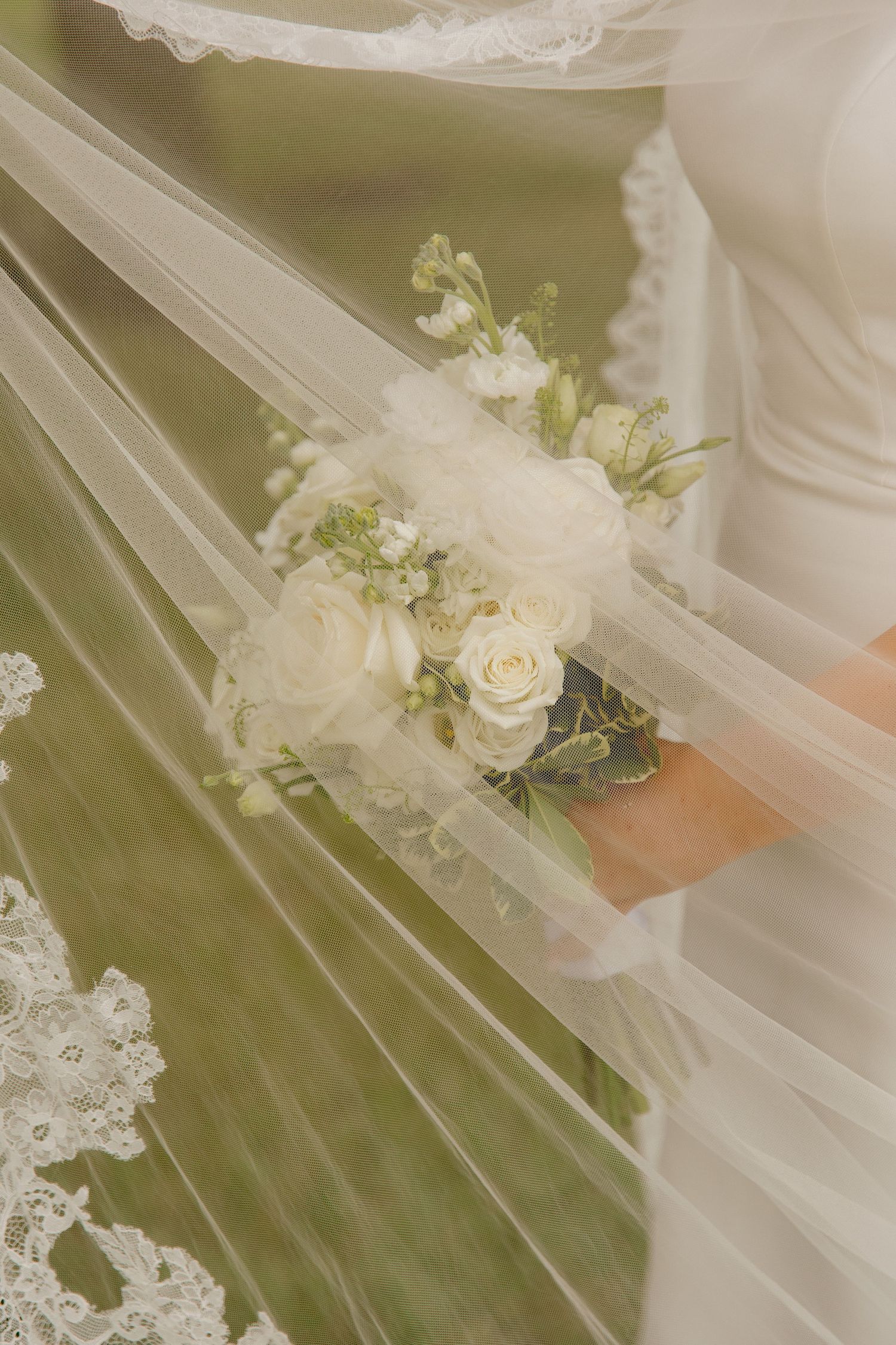Bride holding a white rose bouquet with veil draped elegantly in soft natural light.