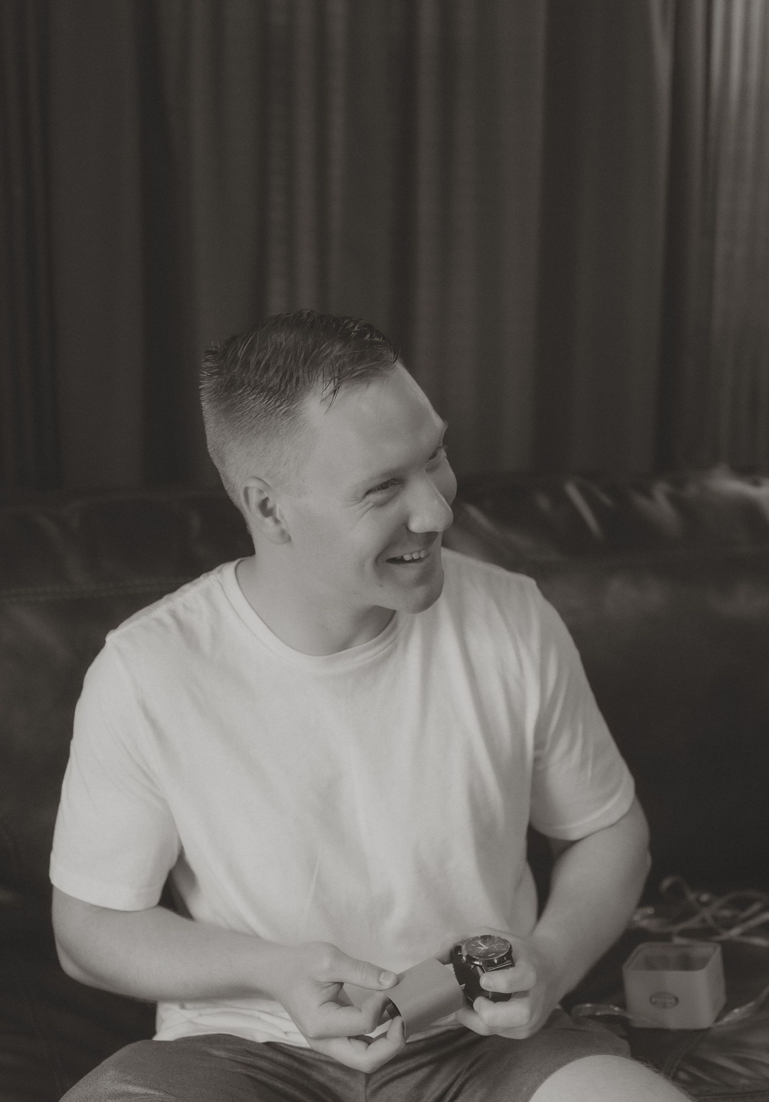 Smiling young man in white t-shirt sitting on leather sofa, black and white portrait photo.